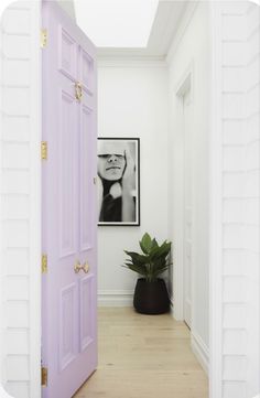 an open door leading to a white room with a plant in the corner and a framed photograph on the wall