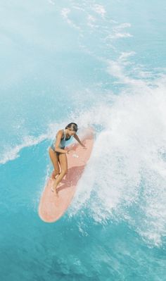 a woman riding a pink surfboard on top of a wave in the blue ocean