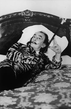 a man laying on top of a bed with an umbrella in his hand and pointing to the side