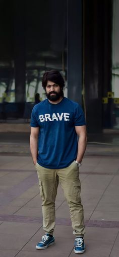 a man standing in front of a building wearing a brave t - shirt and khaki pants