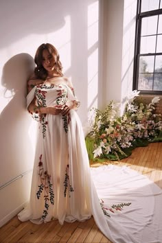 a woman standing in front of a window wearing a white dress with flowers on it