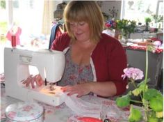 a woman sitting at a table with a sewing machine in front of her and flowers on the table