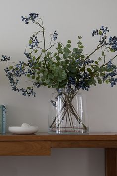 a vase filled with blue flowers sitting on top of a wooden table next to a book