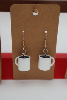 two coffee mugs are sitting in front of each other on a card with earring hooks