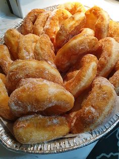 some sugared donuts are in a tin pan on a counter top, ready to be eaten