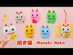 a person holding up some small toys in front of a pink background with the words maneki neko written on it