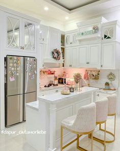 a kitchen with white cabinets and gold trim on the countertop, two stools are in front of the refrigerator