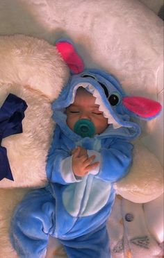 a baby in a blue costume laying next to a stuffed teddy bear wearing a pacifier