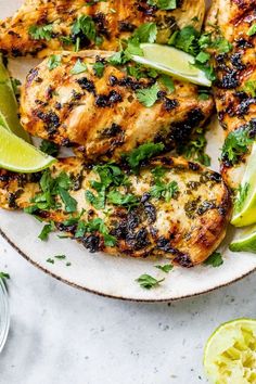 grilled chicken with cilantro and limes on a white plate next to sliced limes