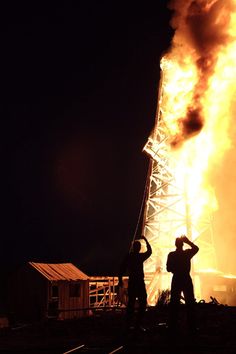 two men standing in front of a large fire