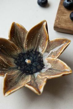 a flower shaped bowl sitting on top of a table next to blueberries and a cutting board