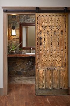 an open door leading to a bathroom with stone walls and wood flooring, along with a sink