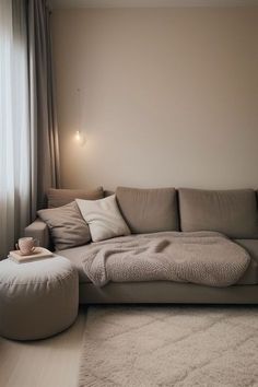 a living room with a couch, ottoman and lamp on the wall next to a window