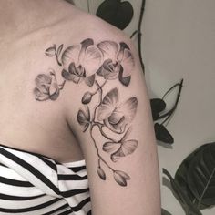 a black and white photo of a woman's shoulder with an orchid tattoo on it