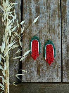 two pairs of red and green beaded earrings sitting on top of a wooden surface