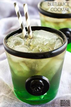 two glasses filled with green liquid on top of a white table cloth and black rimmed straws