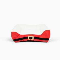 a red and white dog bed with a black stripe on the bottom, in front of a