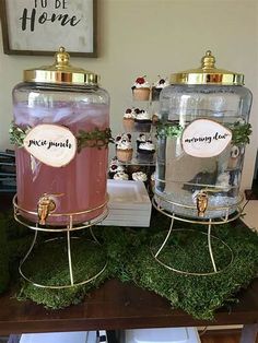 two large jars filled with pink liquid sitting on top of green moss covered ground next to each other