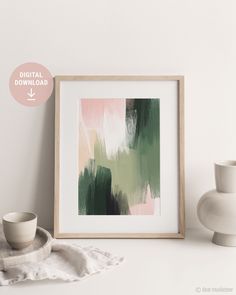 a white vase sitting on top of a table next to a framed art print with green and pink paint