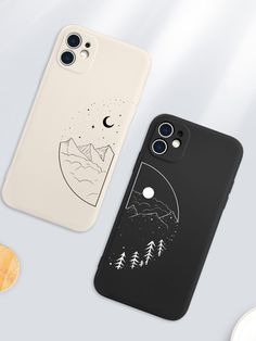 two phone cases sitting next to each other on top of a white surface with trees and mountains in the background