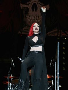 a woman with red hair and black clothes on stage holding her hands up in the air