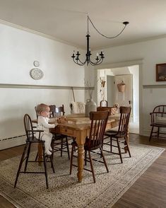 a baby sitting at a wooden table in front of a chandelier and chairs