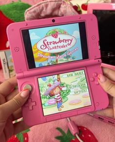 a person holding up a pink nintendo gameboy with strawberry shortcakes on the screen