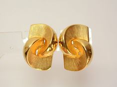 "A beautifully designed clip on earrings dating to the 1960's created by Les Bernard. Rich gold plated geometric swirl clip on earrings of textured shiny and textured swirl earrings/clips is 1 1/4\" long, 3/4' wide.  Marked - Vc. The weight of one earring is 0.4oz.  0.5\" thick. Founded by Bernard Shapiro, son of Harold Shapiro of Vogue jewelry, and Lester Joy, thus the name \"Les Bernard\". Lester Joy was a designer and Bernard Shapiro may have also done some of the designs. Les Bernard manufactured jewelry for Mary McFadden, James Galanos, the Dynasty Collection for the TV show, and Ugo Correani (this pieces could very well be a design for Correani ).  Thank You for visiting our Etsy store https://www.etsy.com/shop/VictoryIssweet !" Luxury Unique Gold Clip-on Earrings, Luxury Gold Metal Clip-on Earrings, Luxury Gold Clip-on Earrings With Polished Finish, Statement Gold Earrings, Les Bernard Jewelry Vintage, Luxury Gold-tone Metal Clip-on Earrings, Vogue Jewelry, Angel Bracelet, Clip On Earring