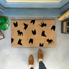 a person standing in front of a door mat with black cats on it and a plant