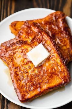 two pieces of french toast on a white plate with butter and syrup drizzled over them