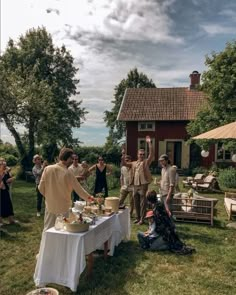 a group of people standing around a table with food and drinks on it in front of a house