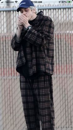 a man standing on top of a skateboard in front of a fence and holding his hands to his face