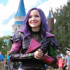 a woman with purple hair and leather outfit standing in front of a castle at disneyland