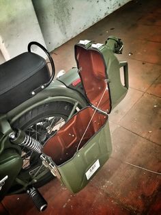 a green motorcycle parked in a garage next to a wall with an open trunk on it's back end