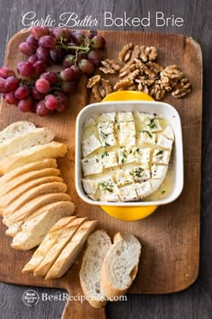 bread, grapes and crackers are on a cutting board with cheese in a bowl