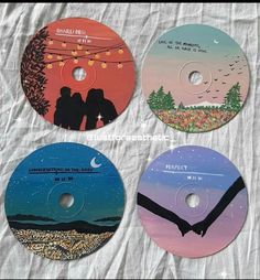 four cds with different designs on them sitting on a white sheeted surface, one has an image of two people holding hands and the other is looking at the sky