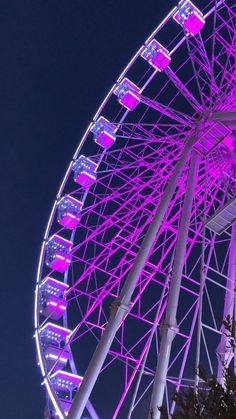 a ferris wheel lit up at night with purple lights on the top and bottom part