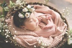 a baby is sleeping in a basket with flowers on her head