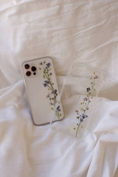 two cell phones sitting on top of a white bed next to each other with flowers painted on them