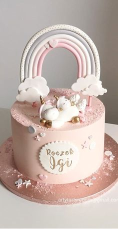 a pink cake decorated with unicorns and a rainbow