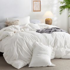 an unmade bed with white comforter and pillows on the floor next to a potted plant