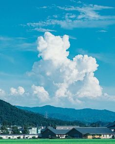 a large cloud is in the sky over some buildings and trees with mountains in the background