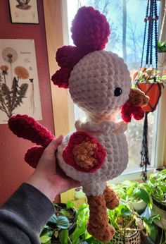 a person holding up a crocheted chicken in front of a potted plant