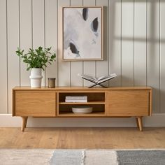 a wooden entertainment center with books and plants on it in front of a white wall