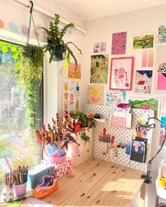 a desk with lots of art on the wall and plants hanging from it's sides