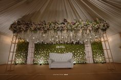 a white couch sitting under a lush green wall covered in flowers and greenery at a wedding reception