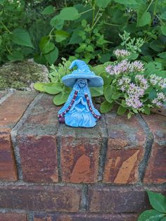 a small blue figurine sitting on top of a brick wall next to flowers