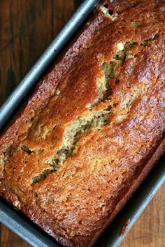 a loaf of banana bread sitting on top of a metal pan next to a wooden table