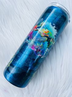 a blue travel mug sitting on top of a white fur covered floor with an ocean scene painted on it