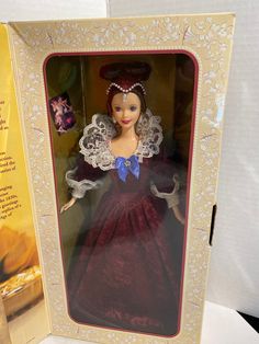 a doll in a box with an open lid and lace on the top, wearing a red dress